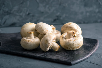 White champignons on the dark kitchen table. Cooking delicious dishes with mushrooms