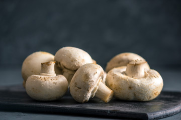 White champignons on the dark kitchen table. Cooking delicious dishes with mushrooms