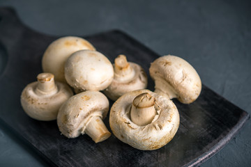 White champignons on the dark kitchen table. Cooking delicious dishes with mushrooms