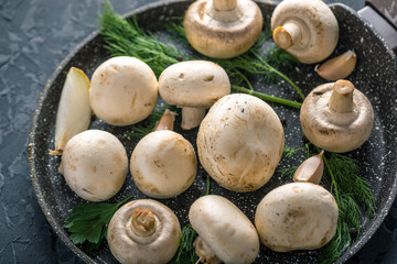 White Champions on the pan and ingredients on the dark kitchen table. Concept of cooking mushroom dishes. Close up