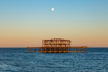 Evening light shining on Brighton's West Pier, with a full moon overhead