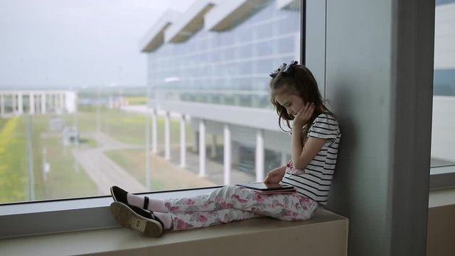 Child at the airport near the window playing a game on the tablet and waiting for time of flight