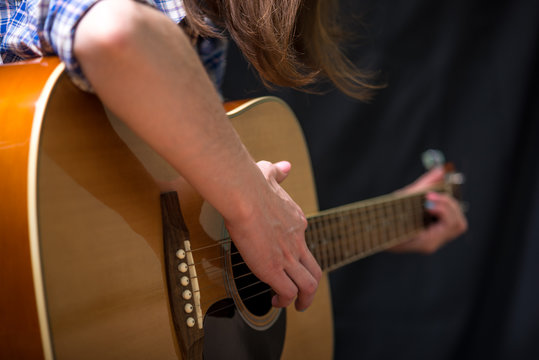 Girl playing an acoustic guitar on a dark background in the Studio. Concert young musicians