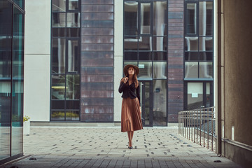 Fashion elegant woman wearing a black jacket, brown hat and skirt with a handbag clutch walking on the European city center.