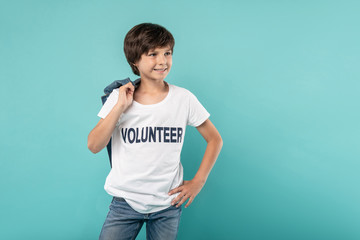 Willing to help. Joyful young boy smiling and holding his jacket