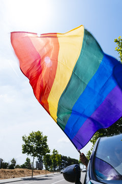 man in a car waving a rainbow flag.