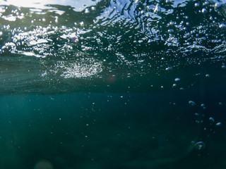 Sea water wave with bubbles closeup underwater photo. Blue sea surface from below. Ripples on sea surface.