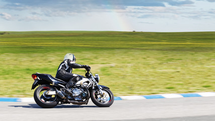 Alone motorcyclist in helmet and leather jacket rides on a country road, enjoying travel and tourism. Green meadows and fields sweep past.