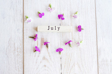 top view of wooden calendar with July sighn and pink flowers.
