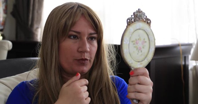 Middle aged depressed sick woman with breast cancer looking at the mirror. Take out her wig