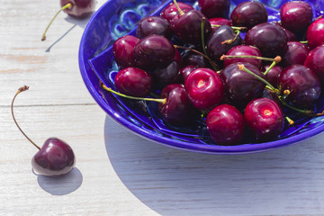 blue plate of ripe sweet cherry on white wooden table