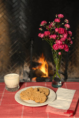 Peanut butter cookies on place setting with milk and flowers in front of fireplace