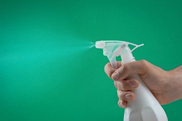 hand squeezing the trigger of a spray bottle spraying water mist on a green background