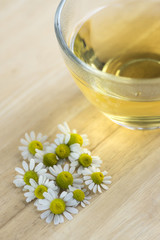 Matricaria chamomilla flowers and trasparent cup of tea on wooden table, fresh flowering herbal medicine
