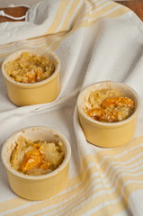Top view, medium distance of three freshly baked, homemade apricot sour cream crumble in yellow ramekins on a yellow striped table cloth
