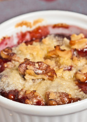 Top view, close up of a white ramekin of freshly baked, hot, cherry, walnut crumble tart