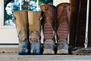 His and hers dirty and mud covered snake hunting boots sitting on doorstep outside.