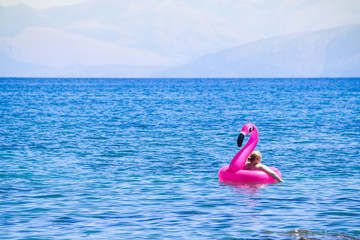 Girl having Fun with Flamingo rubber ring.Women wearing bikinis sitting on a rubber ring. Clear blue sea. Summer holiday