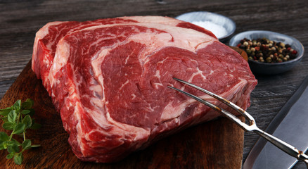 Raw fresh meat Ribeye Steak, seasoning and meat fork on dark background