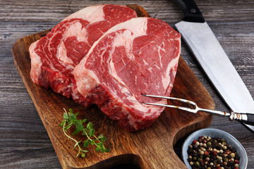 Raw fresh meat Ribeye Steak, seasoning and meat fork on dark background