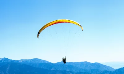 Poster Luchtsport Paraglider zweeft in de lucht over de blauwe bergen