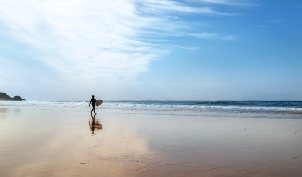 Surfer with surfboard walks on coast line