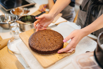 The womans hands hold the workpiece for the cake. Preparation of cakes for Zucher cake on the kitchen table.