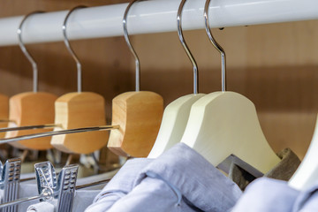 Hangers made of metal and wood with blue shirts and trousers in the closet. close-up
