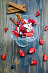 ice cream with strawberries and cinnamon in a vase on a wooden table next to pieces of strawberries