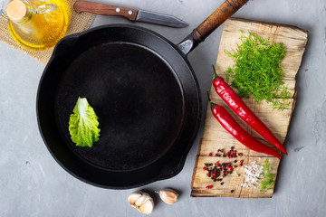 Cooking background concept - empty iron pan, cutting board and spices on a gray stone background. Top view.