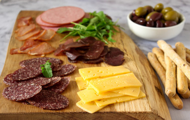 Appetizer table for wine or beer with sausages, dried meat and cheese, served with grissini, herbs and olives.