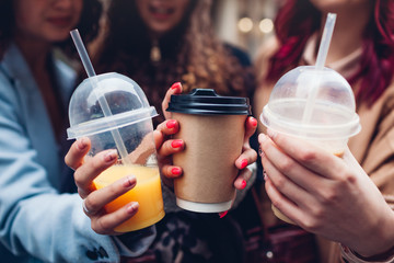 Three female friends having drinks outdoors. Women clinking coffee, orange juice and tea cups