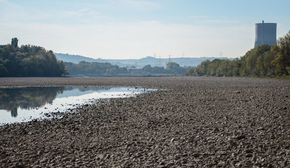 Dry riverbed with stones, visible chimney of a nuclear power plant. River Rhine in Germany.