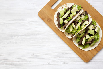 Top view, tortillas with grilled beef and avocado on the bamboo board on a white wooden surface. From above. Copy space.