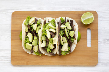 Tortillas with grilled beef, avocado and lime on the bamboo board over white wooden surface. From above, top view.