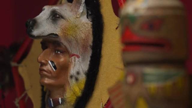 Focus pull between a native american totem and the figure of a chief wearing a wolf ornament.