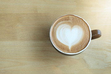 Latte art coffee in the morning time with sunlight on table wooden background.