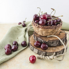 ciliegie rosse fresche in cestino su tronchi di legno in foto quadrata con strifinaccio verde