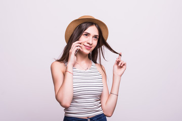 Portrait of a smiling young woman in summer dress and straw hat talking on mobile phone isolated over white background