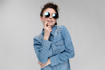 Young brunette girl in round glasses. Hairs are gathered in a bun. The girl put her hand to her chin.