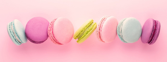 The row of colorful macarons on pink background. Top view. Banner.