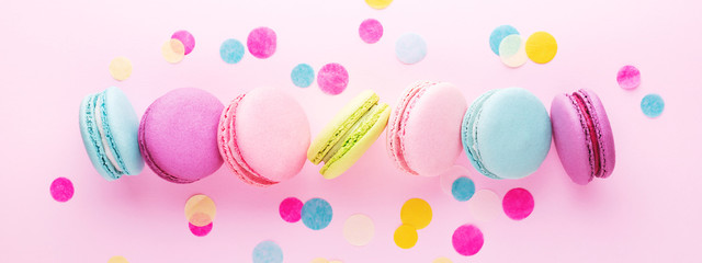 The row of colorful sweet macarons on pink background decorated with confetti. Top view, minimal,...