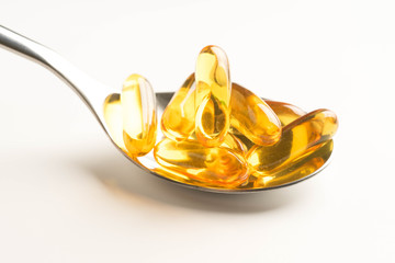 fish oil capsules in a spoon on white