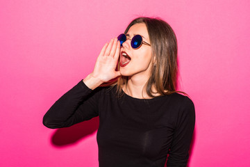 Close up portrait of cute charming girl side holding hand near mouth and scream, looking at side with eyes, standing over pink background