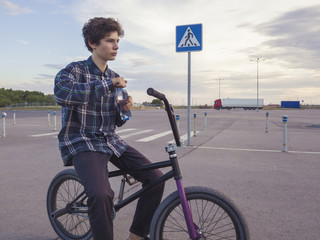 portrait of young teenage boy drinking bottled water sitting on bmx bicycle
