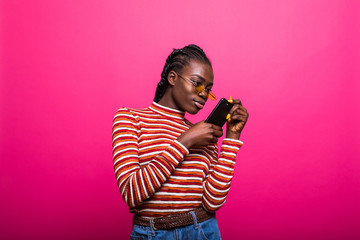 Beauty happy african woman looking at phone and writing message isolated pink background.