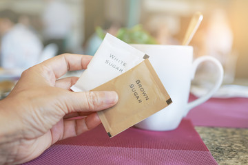 brown sugar packet in hand with blurred coffee cup in coffee shop