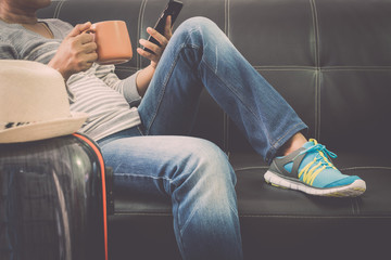 Female traveller is relaxing on leather sofa holding mobile phone and coffee cup at the airport.