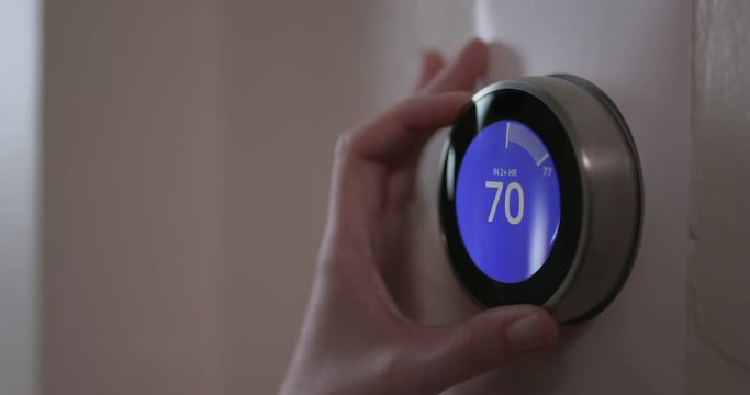 Woman Turning Down Temperature of Smart Thermostat Gadget At Home - Close