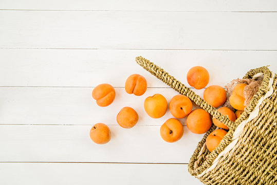apricots falling from the basket on white wooden background flat lay top view